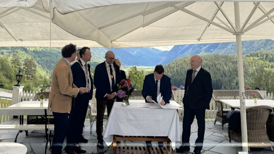 statsekretær  en signerer avtalen utendørs under store parasoller med ordfører til stede.