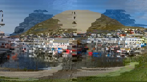 liten fiskelandsby i finnmark med fiskebåter i forgrunn og blå himmel.